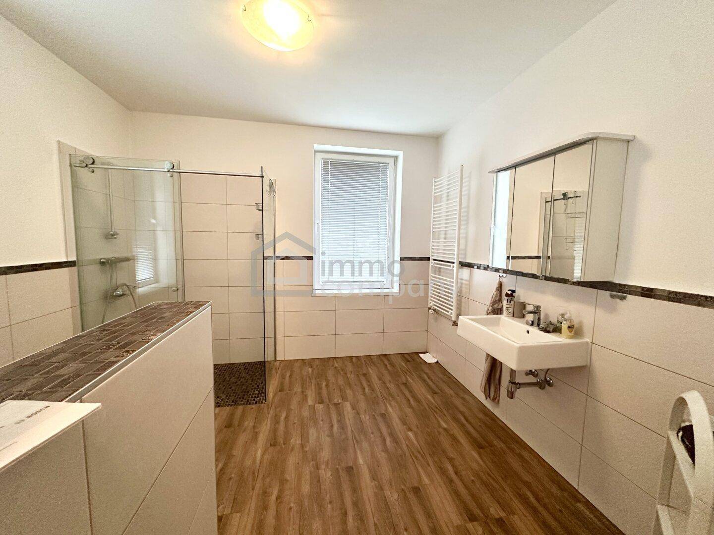 Modernisiertes Badezimmer mit Dusche, Waschbecken, Fenster und beheiztem Handtuchhalter.