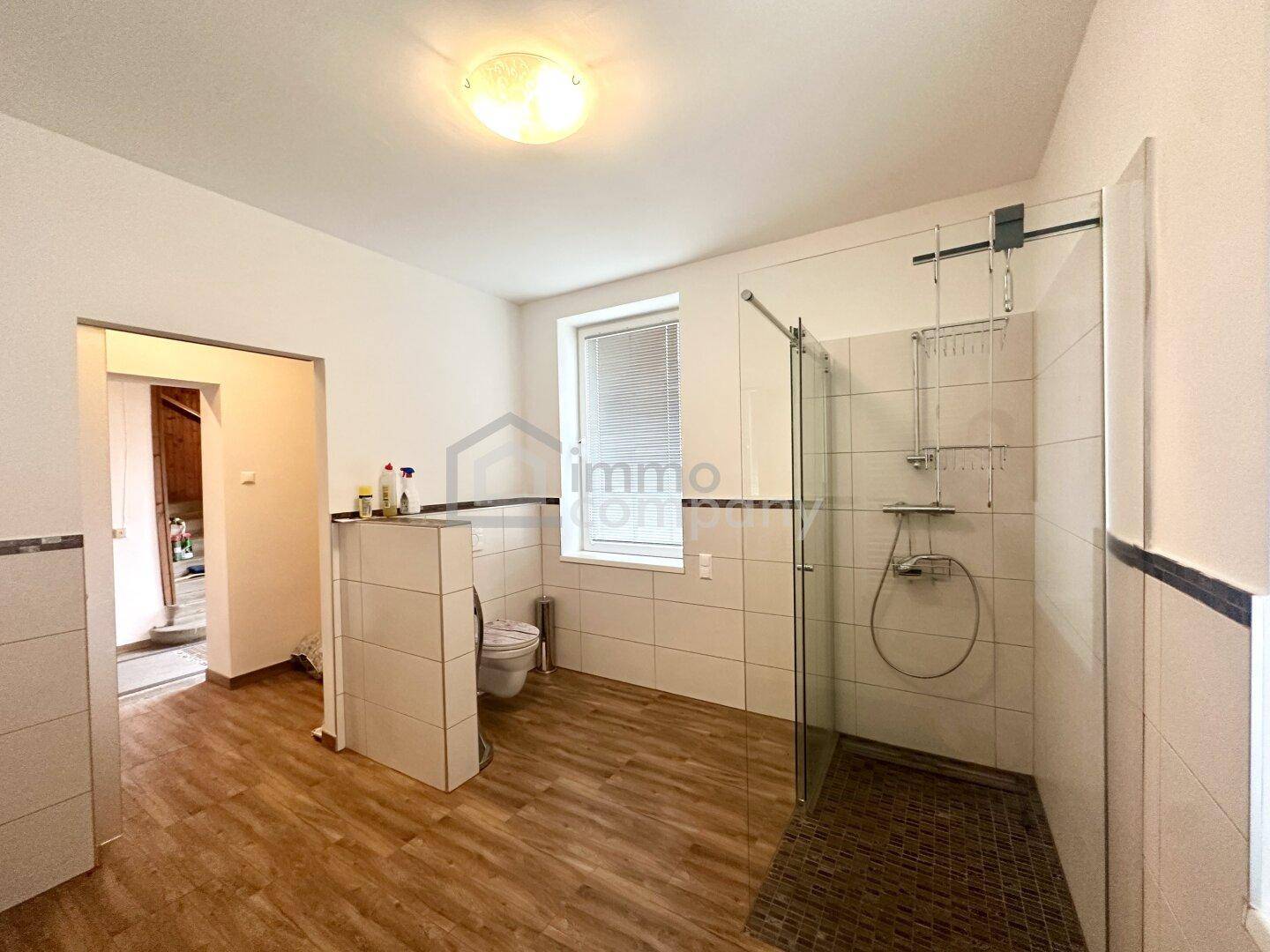 Geräumiges Badezimmer mit ebenerdiger Dusche, WC und Fenster für natürliche Belüftung.