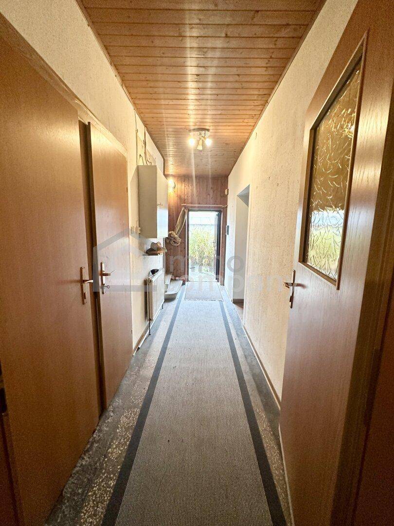 Langer Flur mit Holzdecke, Teppichboden und Türen zu verschiedenen Räumen.