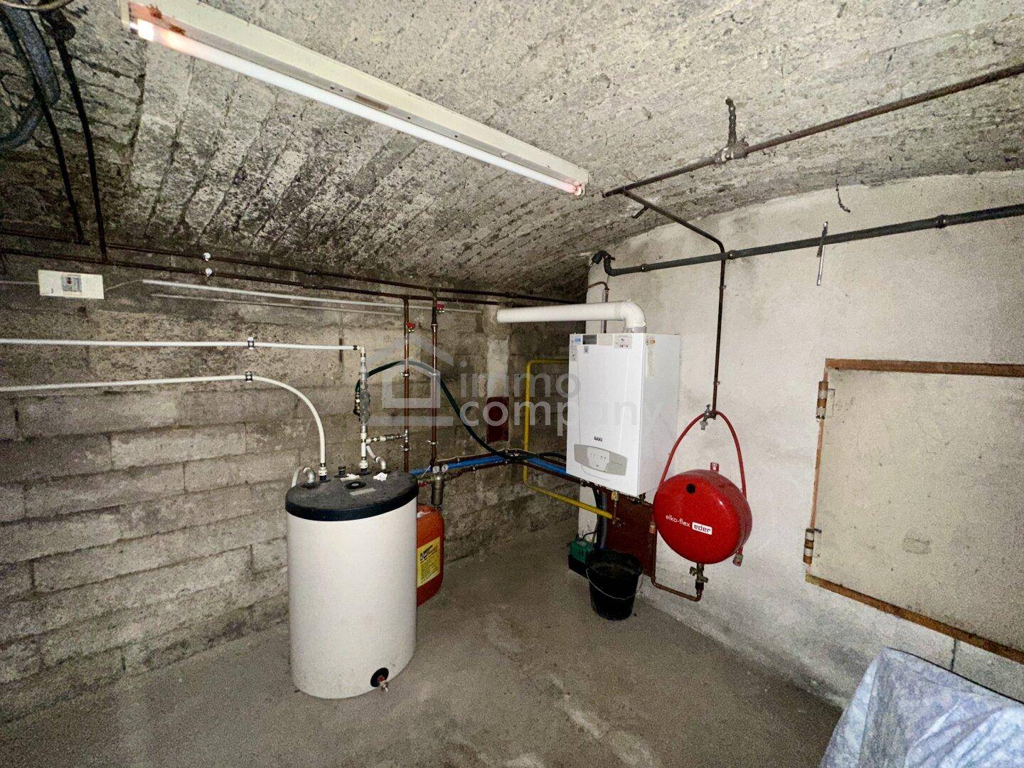 Heizungsraum im Keller mit Gastherme, Warmwasserspeicher und freiliegenden Rohren.