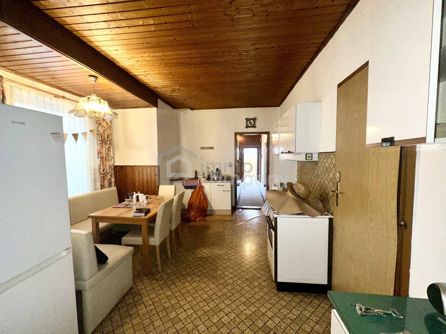 Wohnküche mit Essbereich, Holzdecke und älteren Küchenmöbeln.