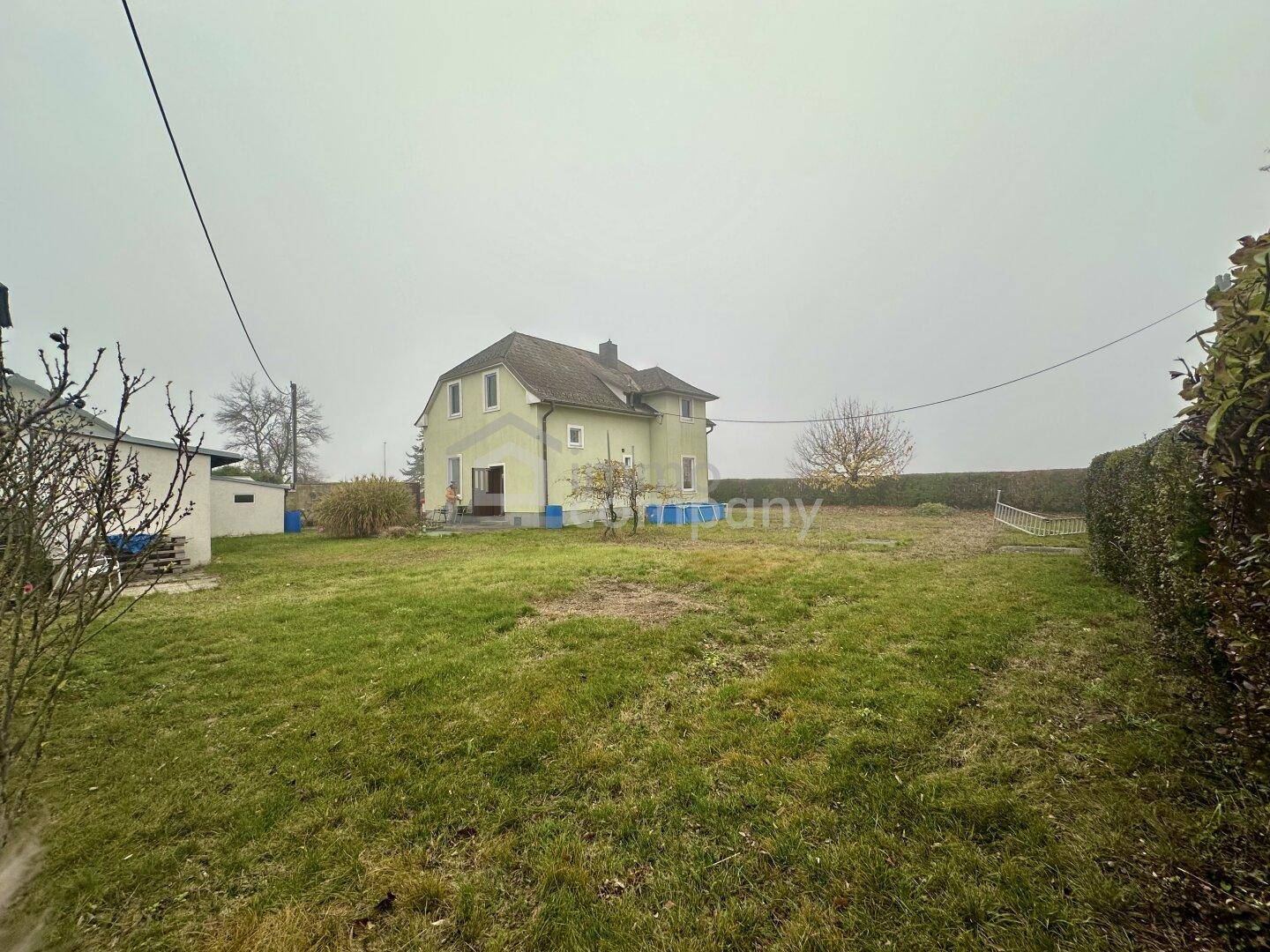 Rückansicht des Hauses mit weitläufigem Garten und grüner Rasenfläche an einem bewölkten Tag.