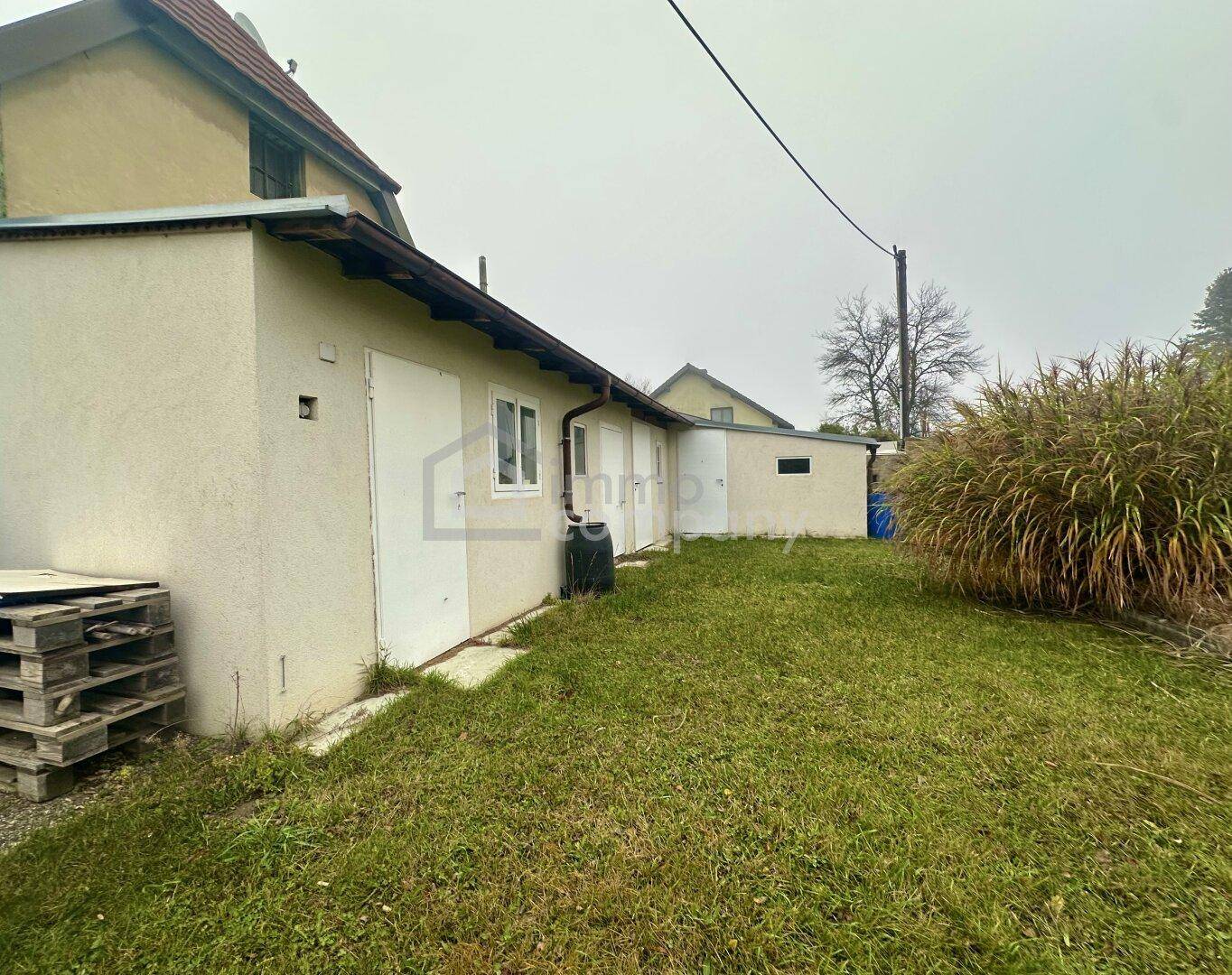 Nebengebäude im Garten mit mehreren Türen und einer kleinen Rasenfläche.