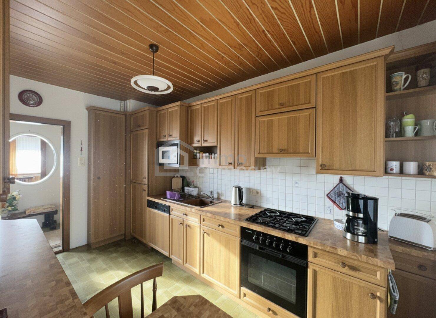 Funktionale Küche mit Holzschränken, Gasherd und integrierten Geräten unter einer Holzdecke.