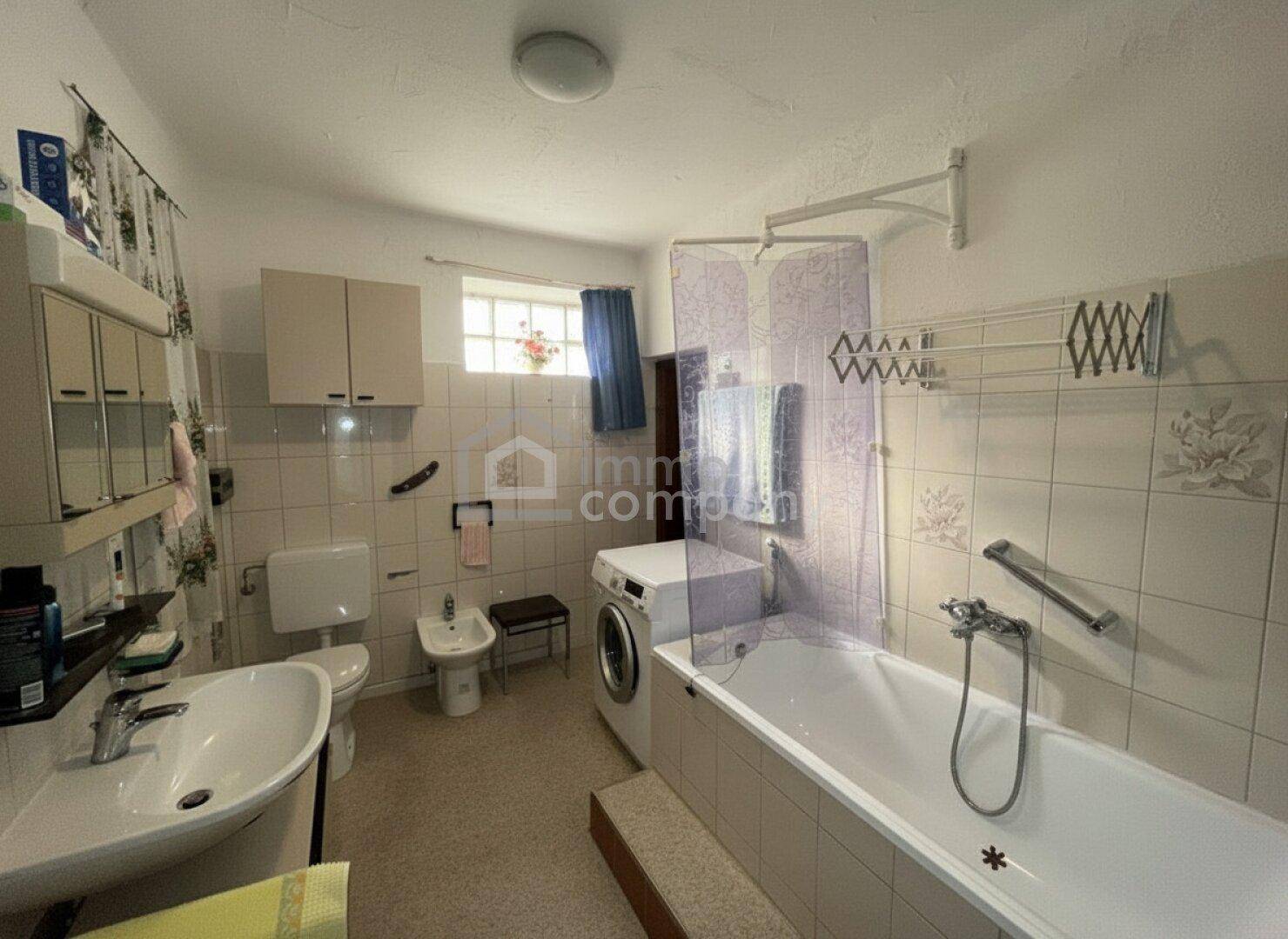 Helles Badezimmer mit Badewanne, Waschbecken, Bidet und Fenster für natürliche Belüftung.