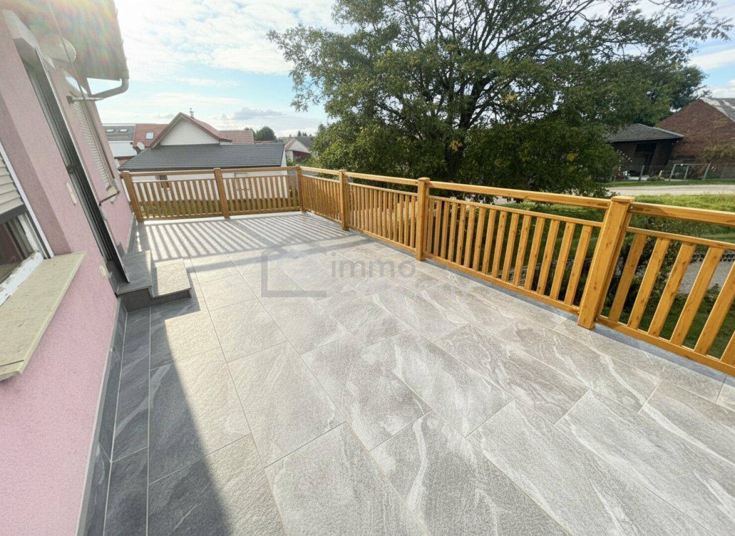 Große, neu geflieste Terrasse mit Holzgeländer und Blick ins Grüne.