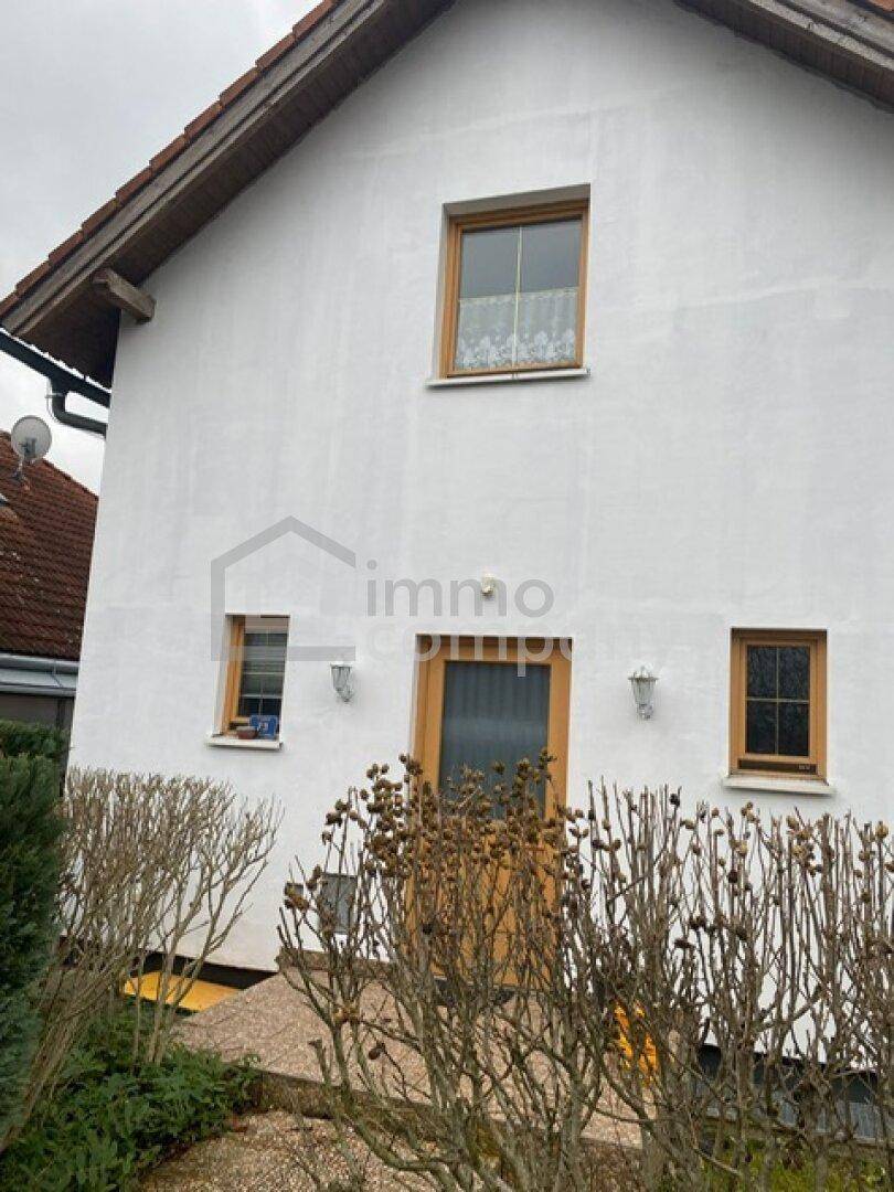 Vorderansicht des Hauses mit weißer Fassade, Holztür und gepflegter Hecke im Vorgarten.