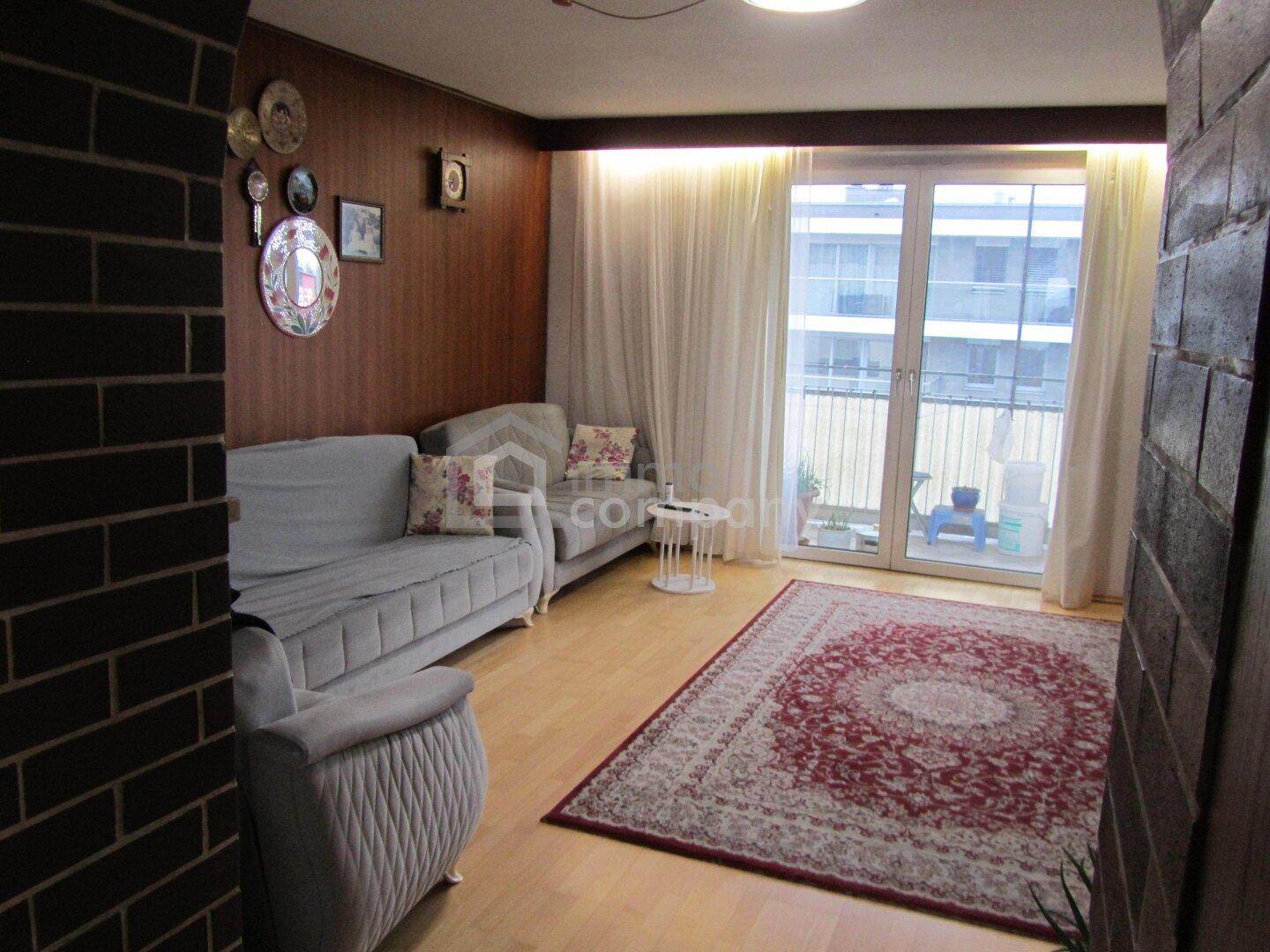 Gemütliches Wohnzimmer mit Holzwänden, hellen Sofas und Zugang zu einem Balkon, das viel Tageslicht erhält.