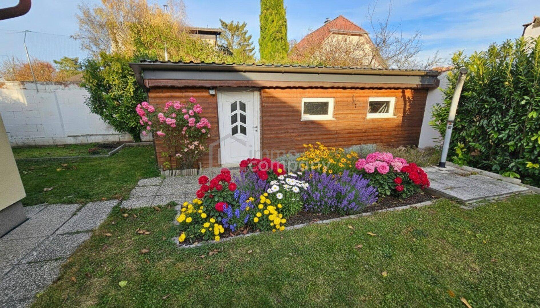 Gepflegter Garten mit bunten Blumenbeeten, Rasenfläche und einem Holzschuppen.