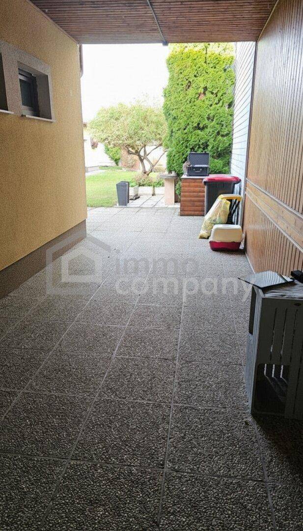 Überdachter Außenbereich mit Fliesenboden und Blick in den hinteren Gartenbereich.