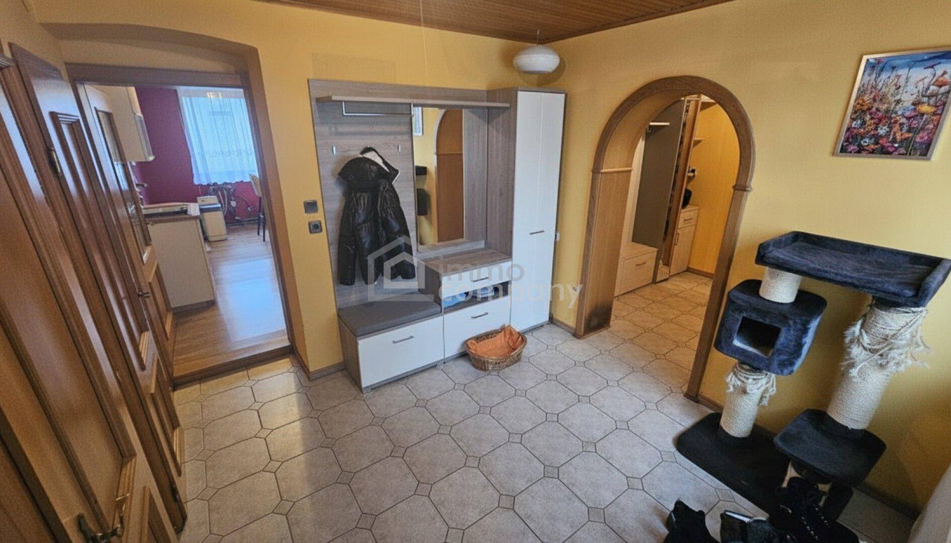 Heller Eingangsbereich mit Fliesenboden, Garderobe und Holzakzenten an den Wänden.