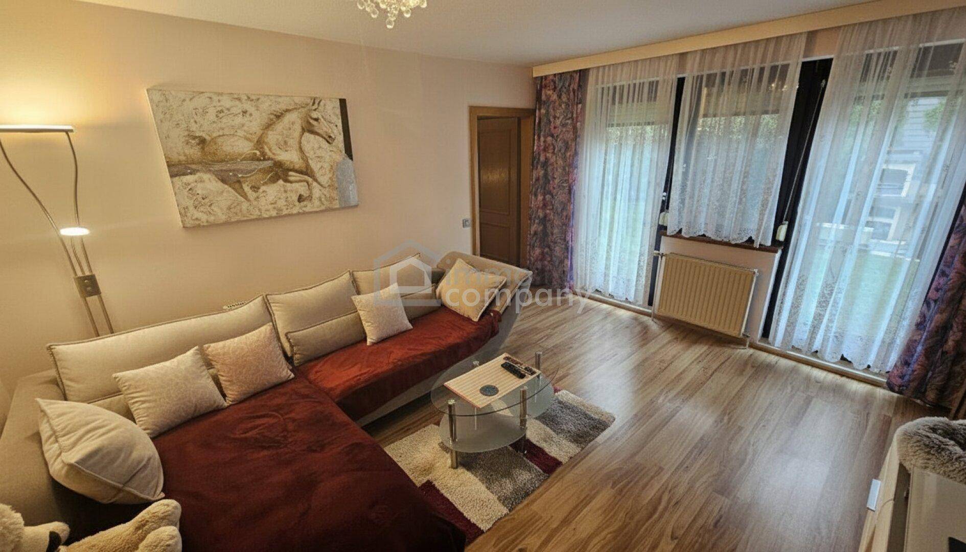 Gemütliches Wohnzimmer mit Laminatboden, großem Ecksofa und Zugang zum Balkon.