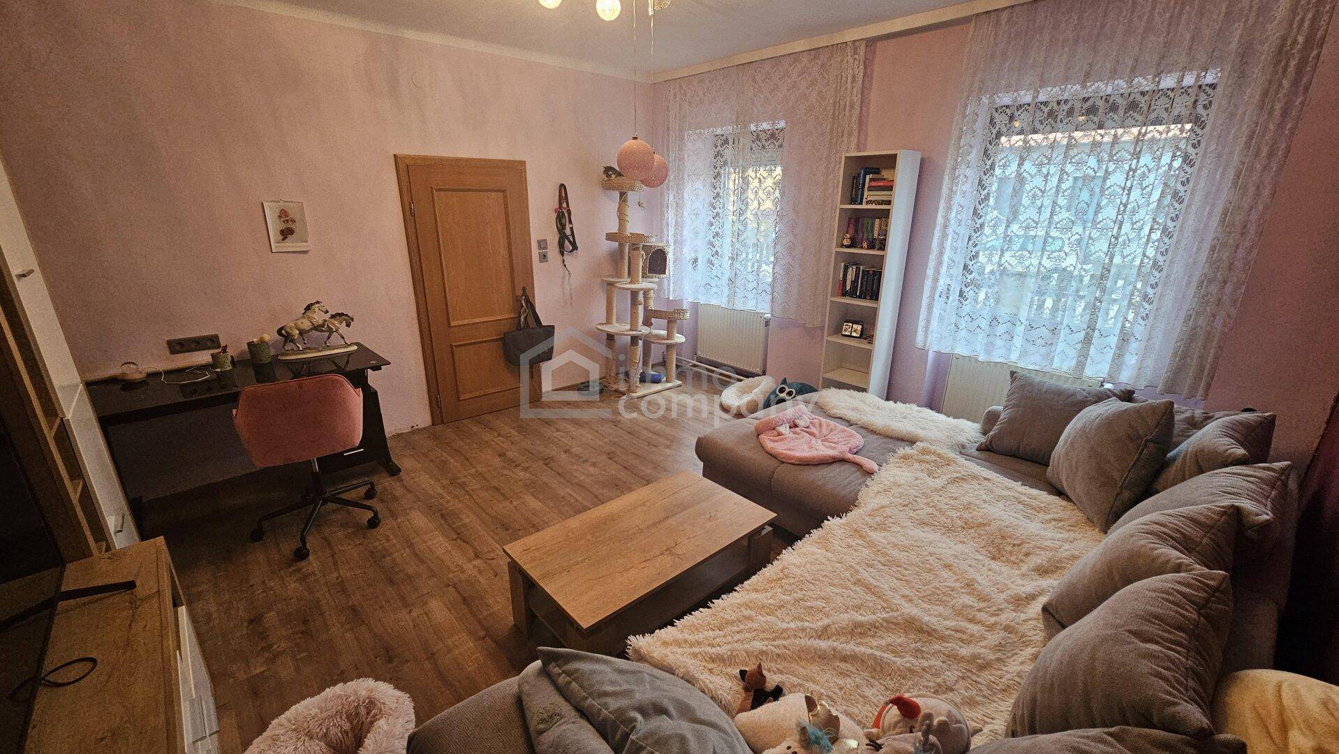 Geräumiges Wohnzimmer mit Laminatboden, großem Sofa und einem Arbeitsbereich.