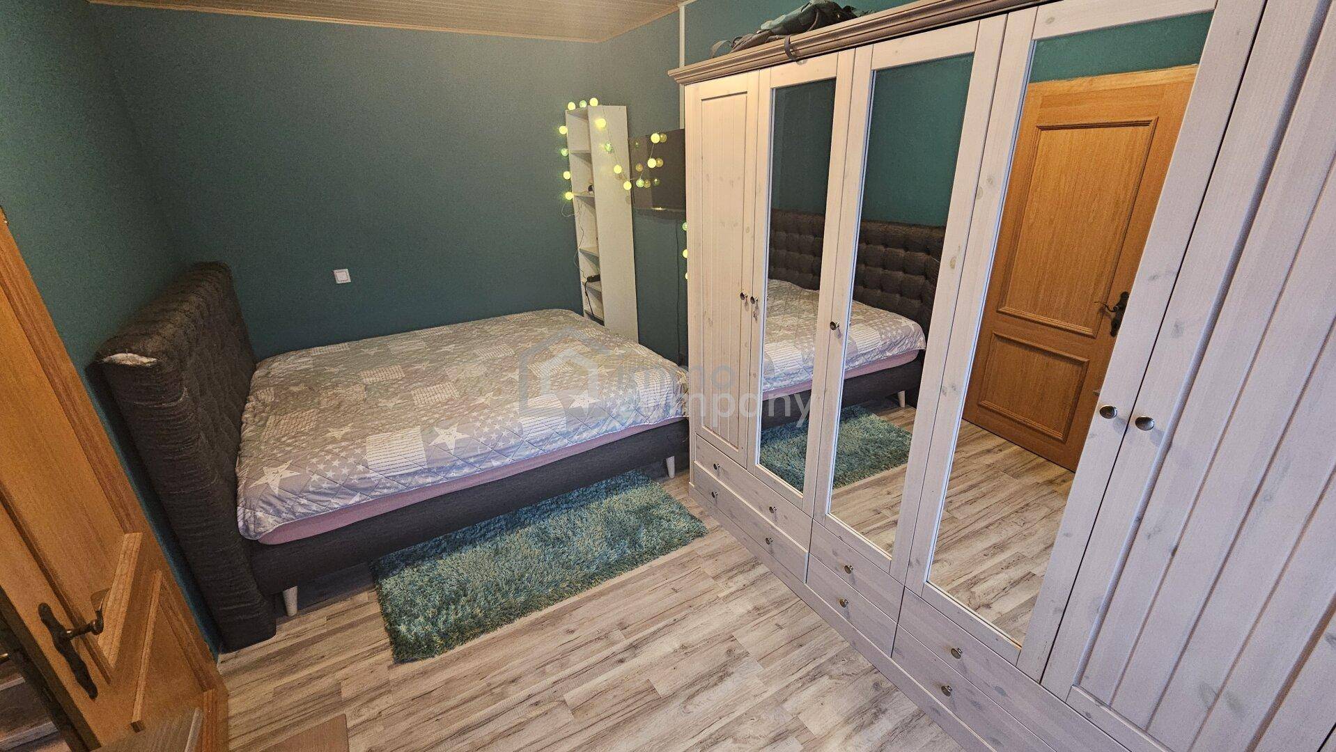 Schlafzimmer mit Laminatboden, Doppelbett und einem großen Spiegelschrank.