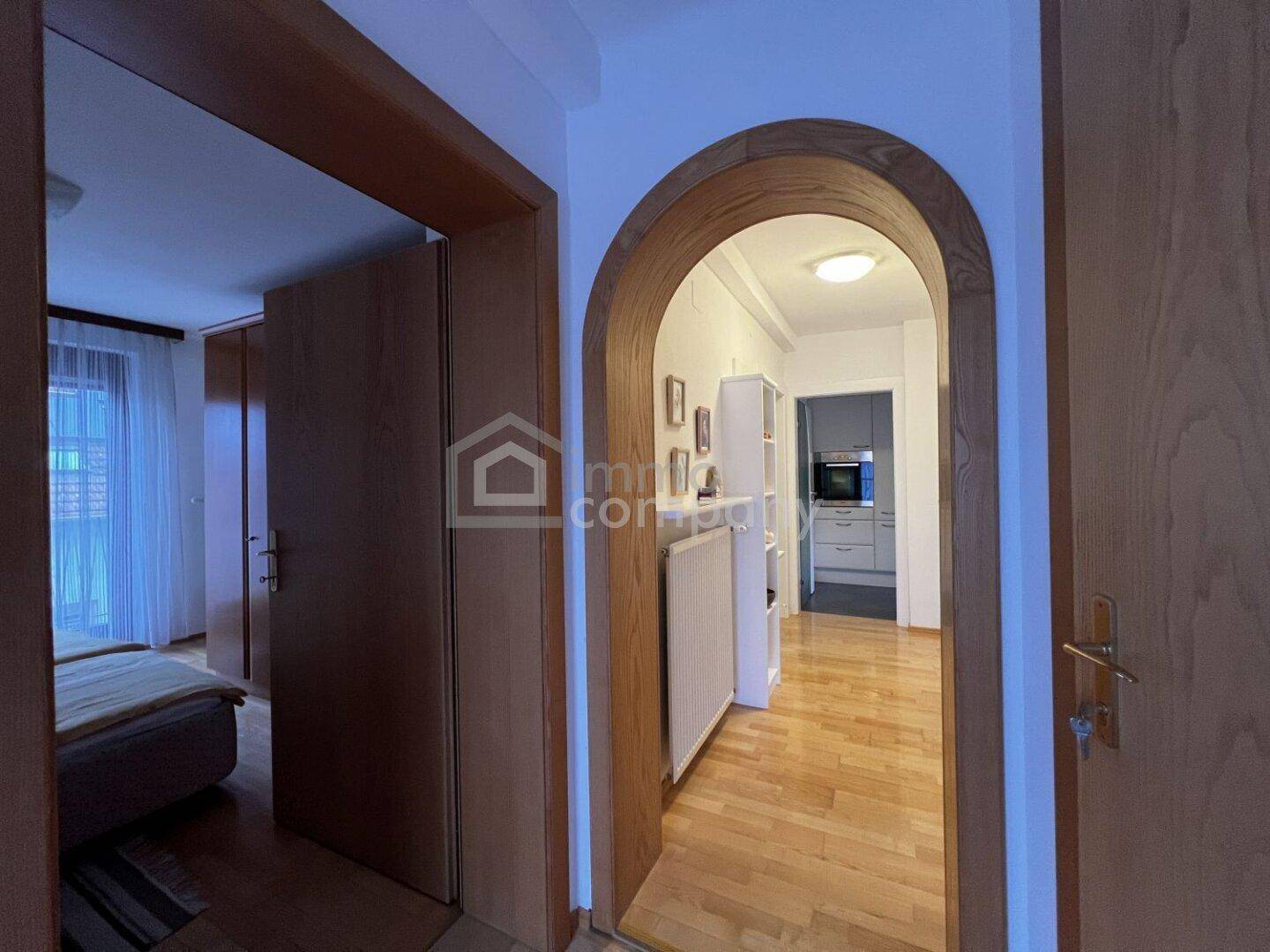 Heller Flur mit Holzboden und Rundbogen, der zur Küche führt.