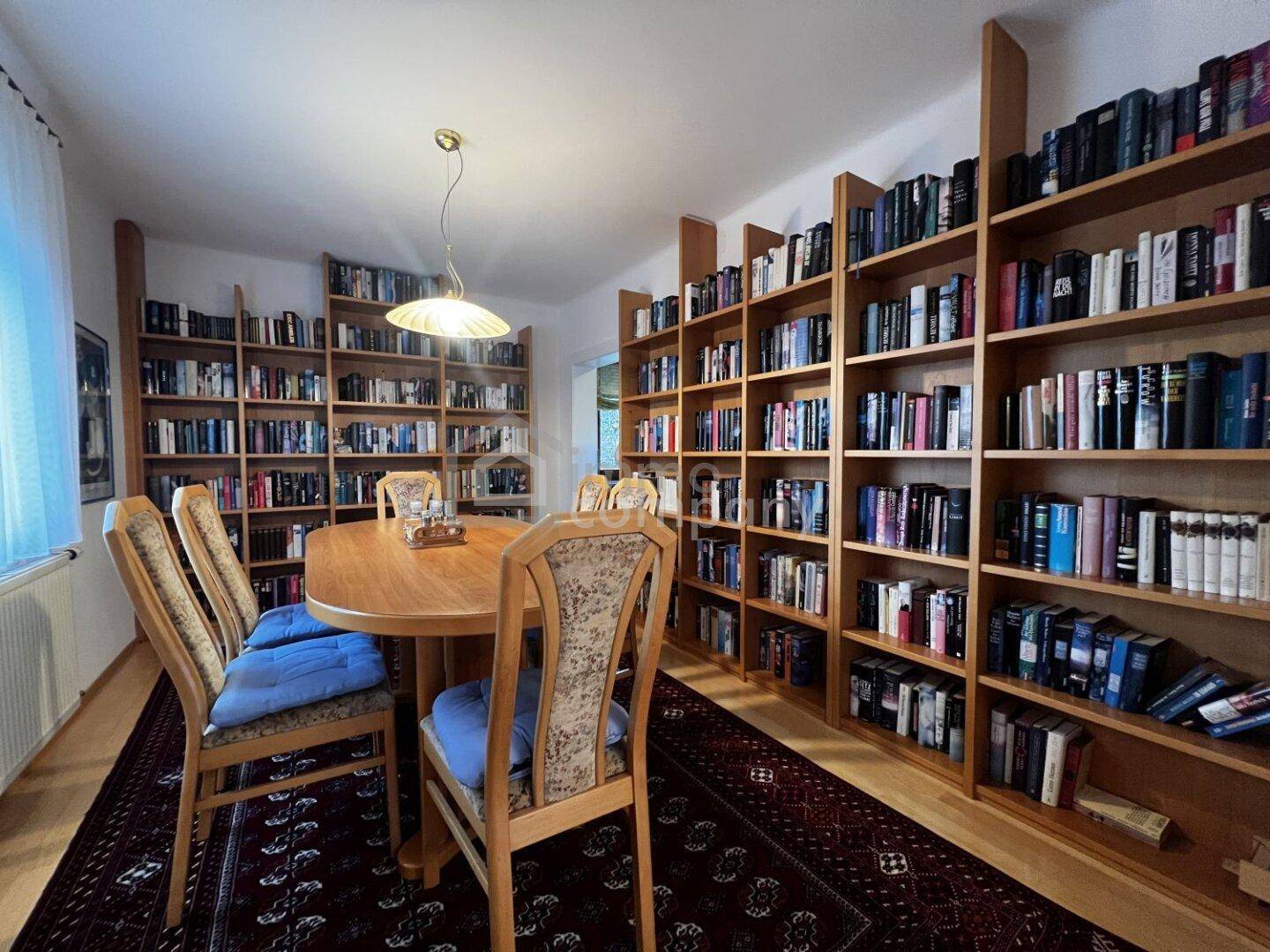 Geräumige Bibliothek mit vielen Büchern, Holztisch und Teppichboden.