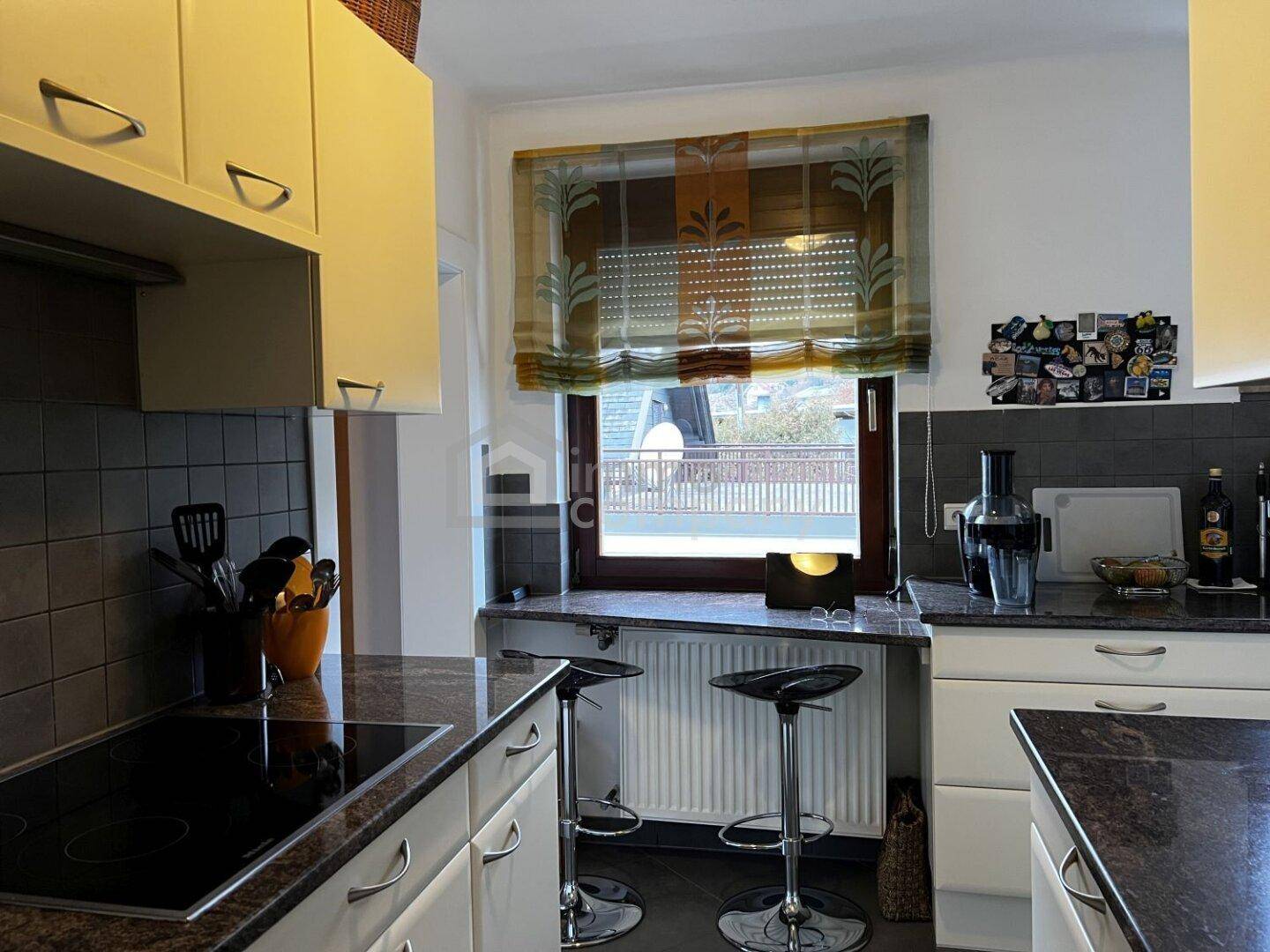 Küche mit Granitarbeitsplatten, Induktionskochfeld und Barhockern am Fenster.