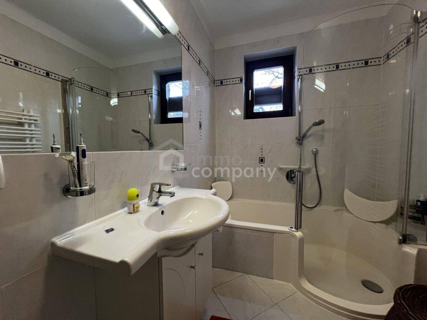 Helles Badezimmer mit Badewanne, Dusche, Fenster und weißen Fliesen.