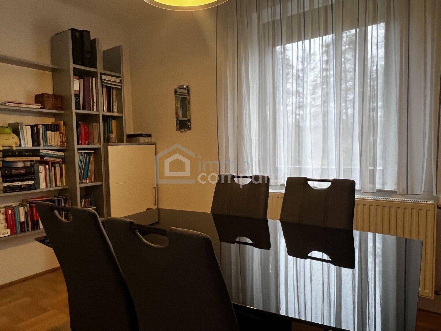 Esszimmer mit modernem Esstisch, Stühlen und Bücherregal im Hintergrund.