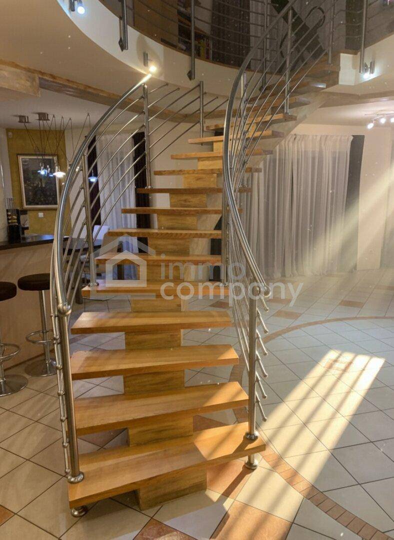 Elegante Wendeltreppe aus Holz und Edelstahl in einem hellen, gefliesten Eingangsbereich.