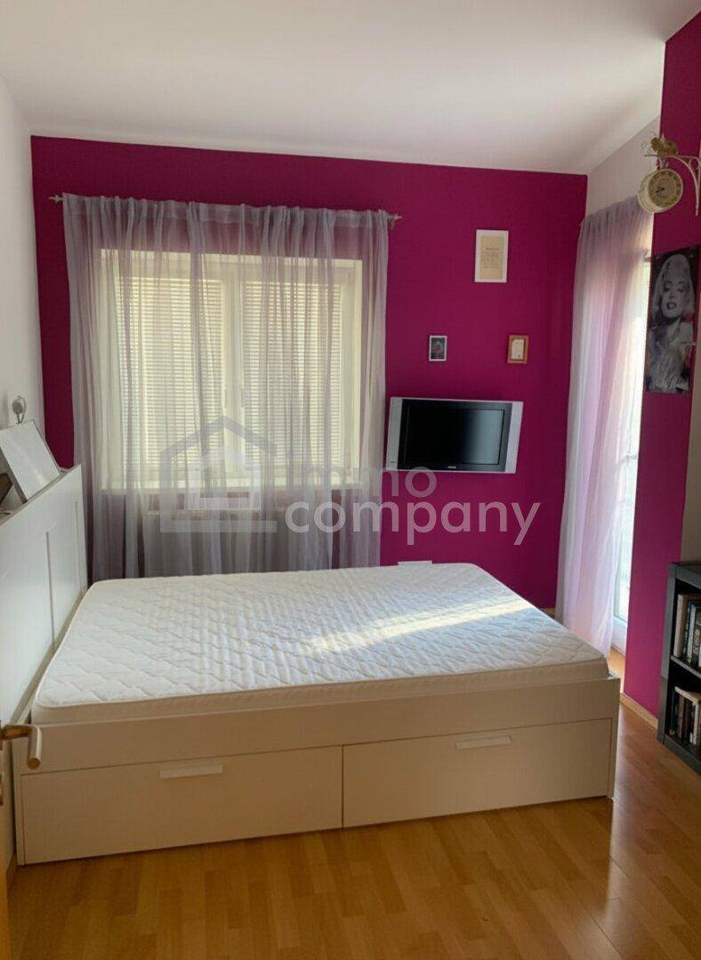 Helles Schlafzimmer mit Doppelbett, Holzfußboden und einer farbigen Akzentwand in Magenta.