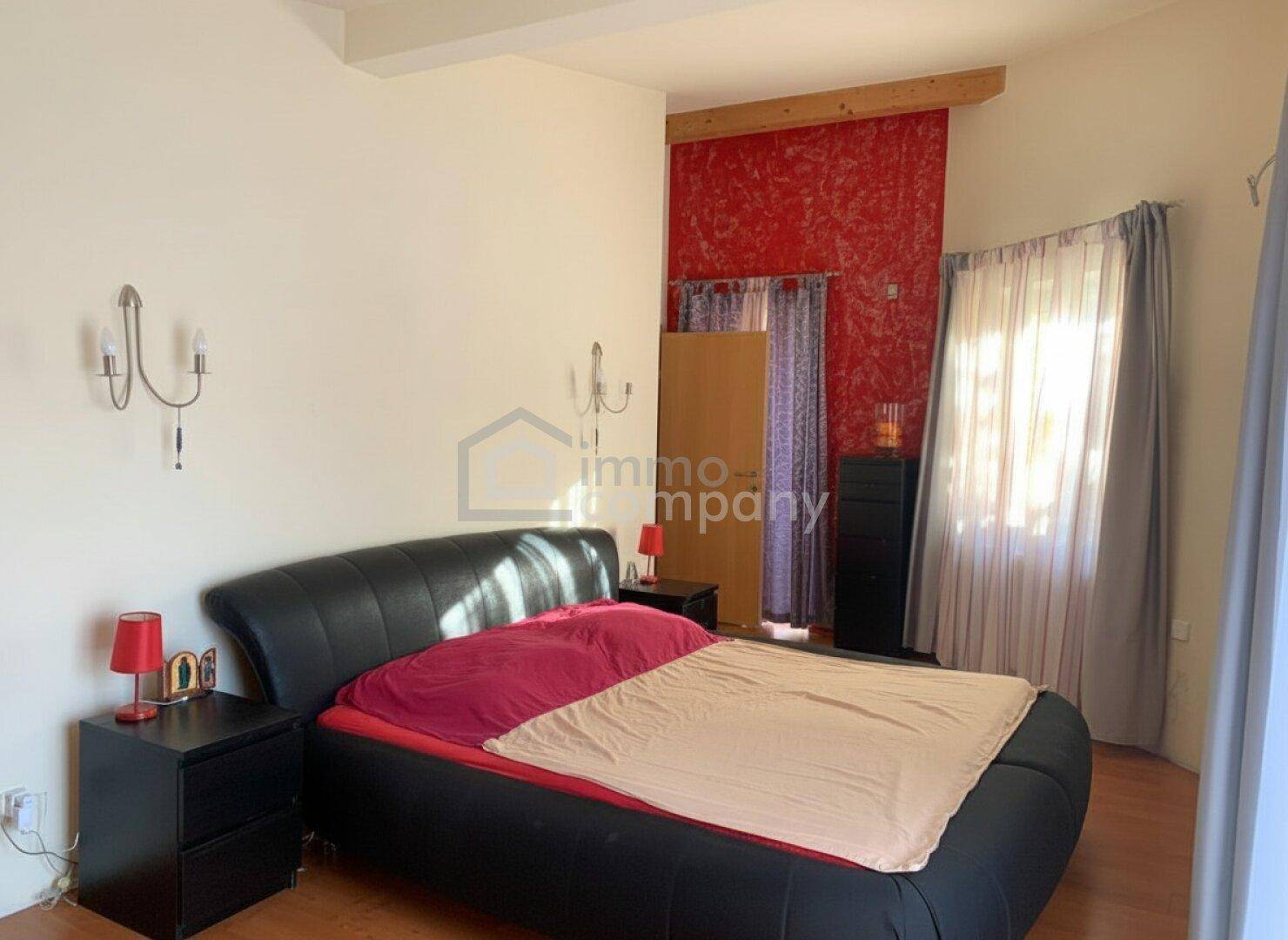 Geräumiges Schlafzimmer mit großem Doppelbett, Nachttischen und einer roten Akzentwand.