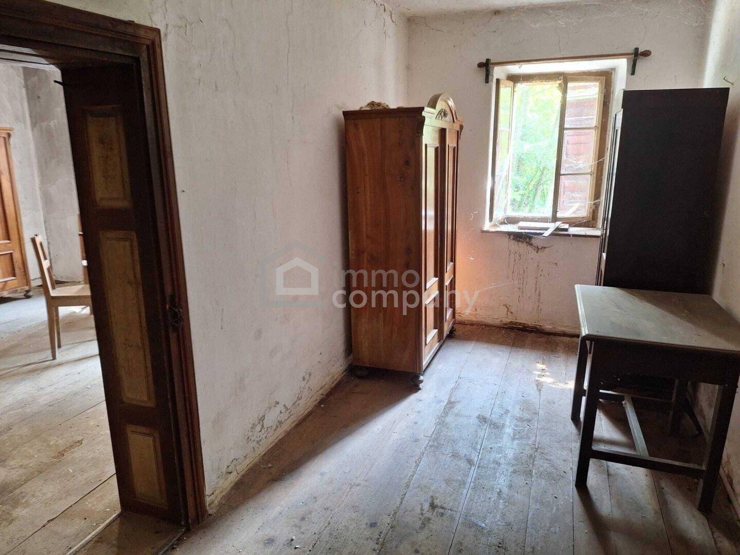 Einfaches Zimmer mit Holzdielenboden, altem Schrank und Blick ins Grüne.