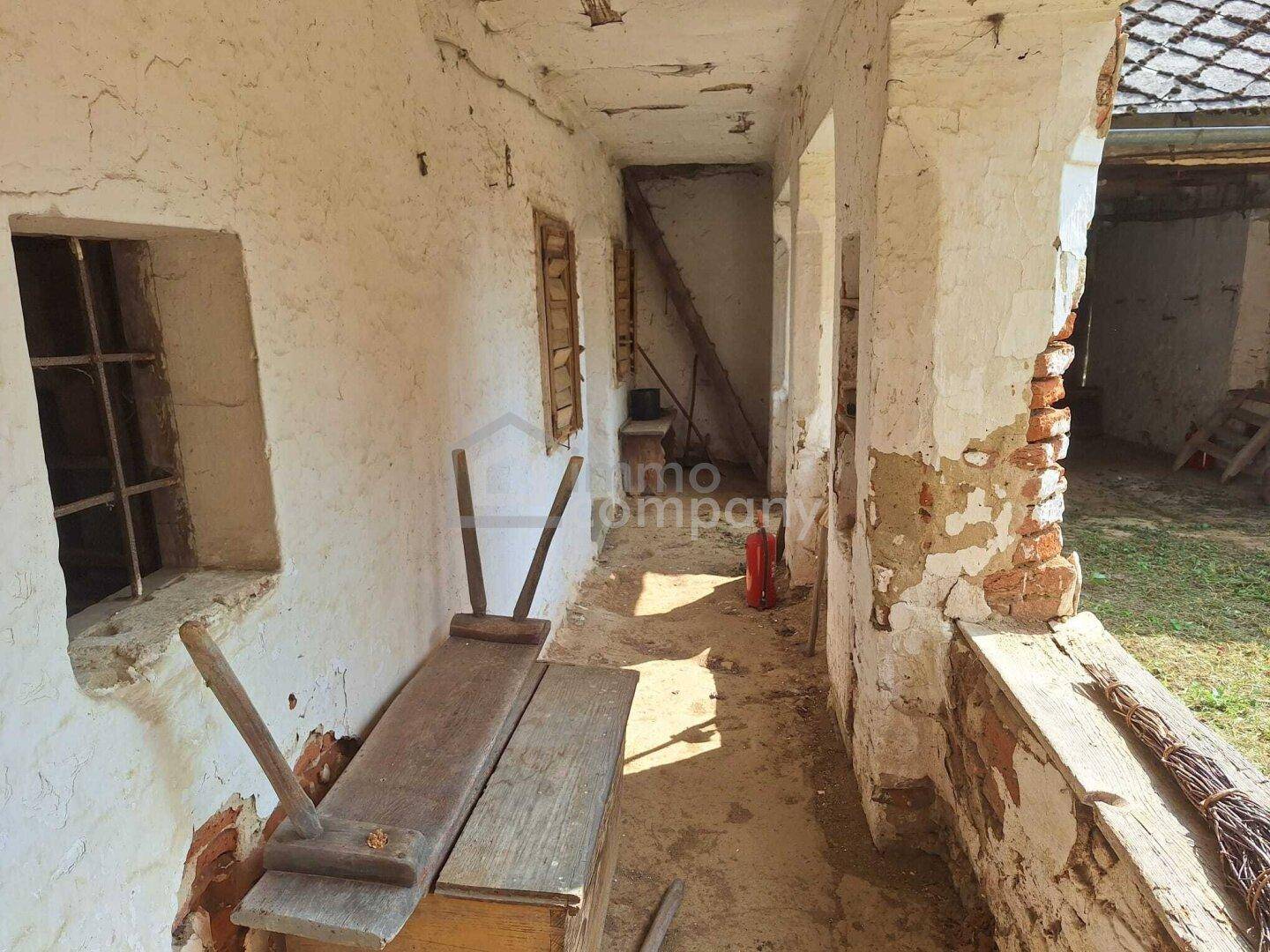 Überdachter Gang oder Veranda mit sichtbaren Putzschäden und rustikalen Holzbänken.