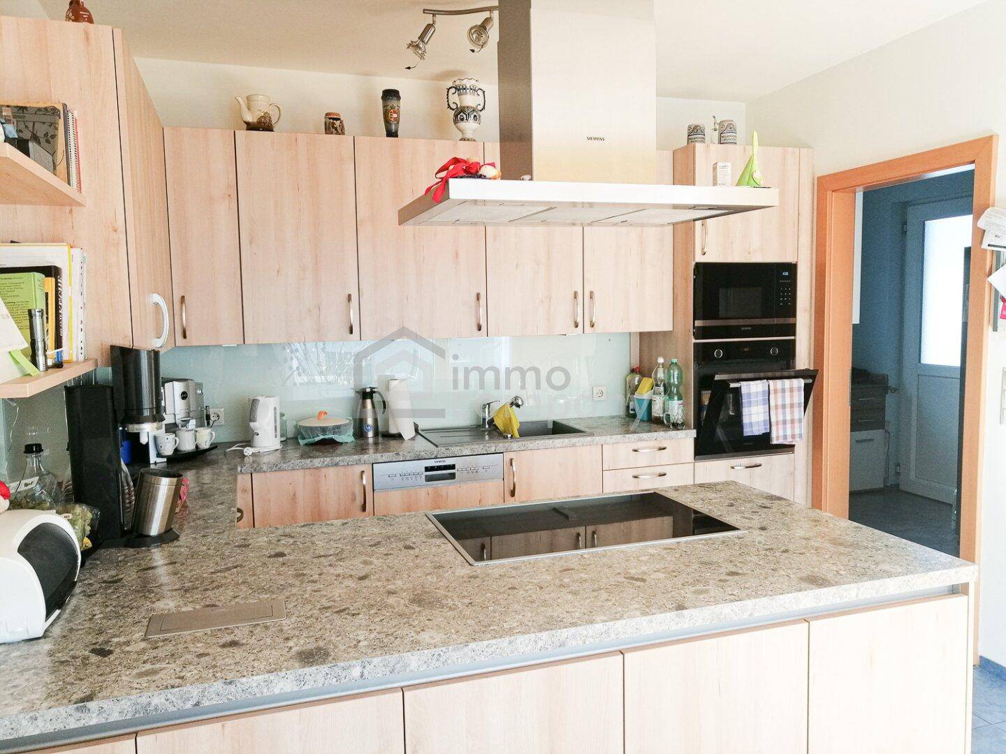 Moderne Einbauküche mit heller Holzoptik, Granitarbeitsplatte und integrierten Geräten von Siemens.