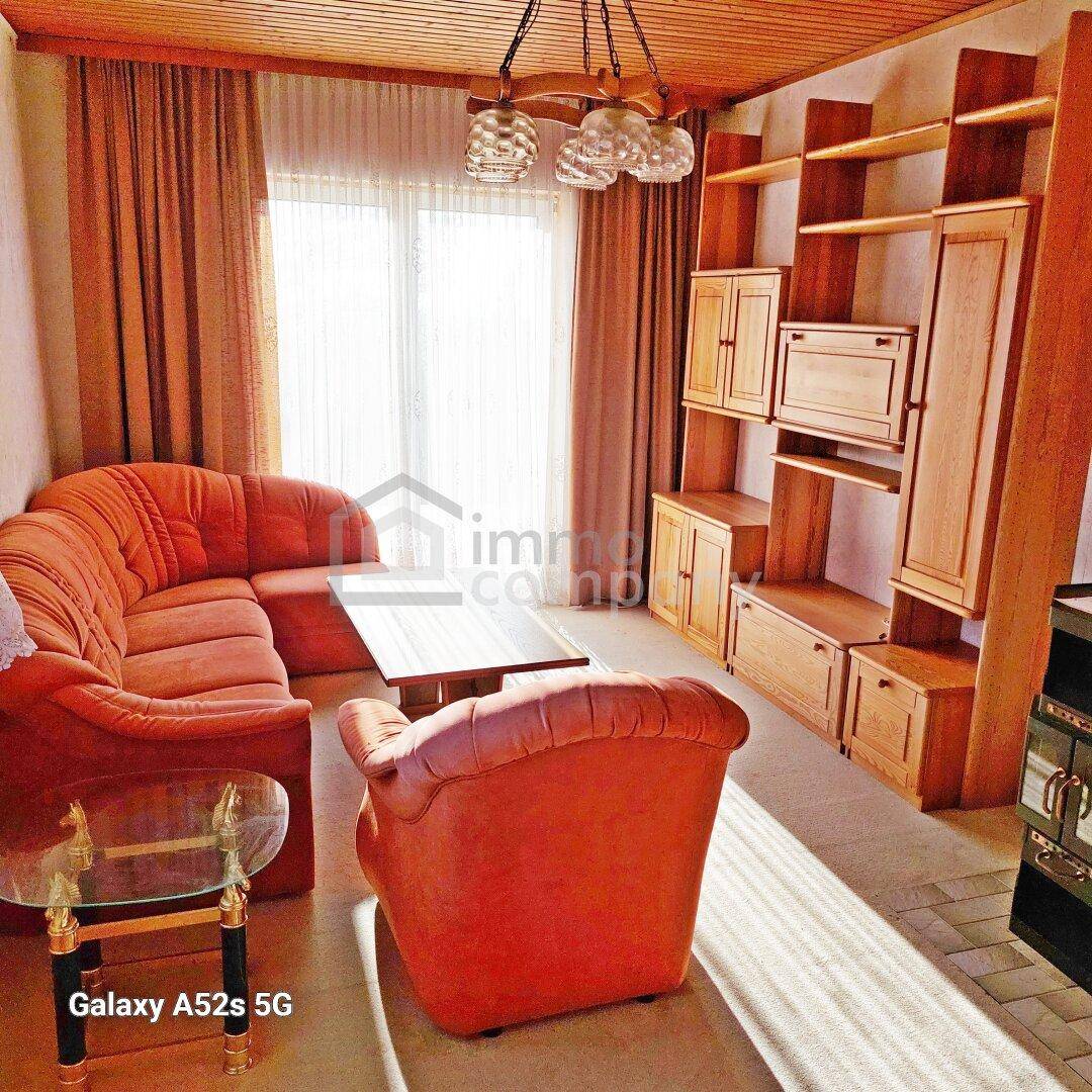 Gemütliches Wohnzimmer mit Holzdecke, orangefarbenen Möbeln und großem Fenster.