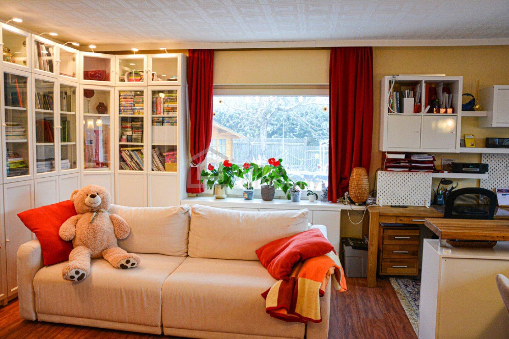 Gemütliches Wohnzimmer mit Sofa, Bücherregalen und großem Fenster mit Blick ins Grüne.
