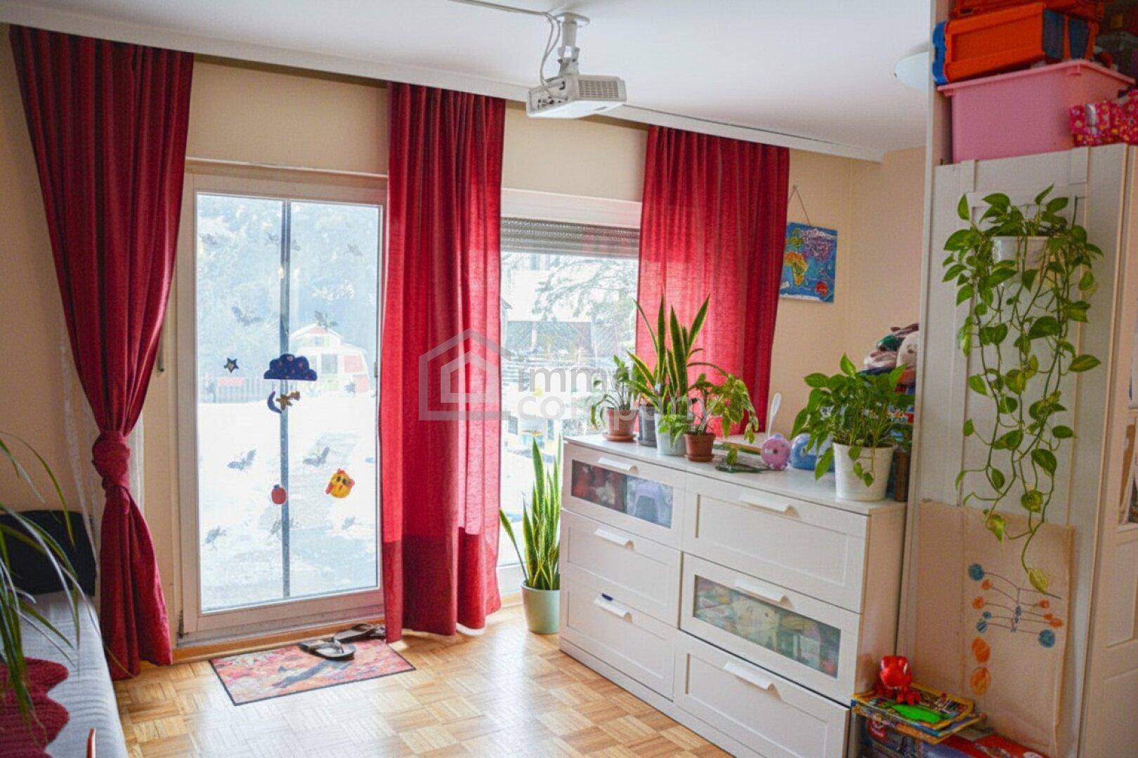 Heller Raum mit Terrassenzugang, Holzfußboden und dekorativen Pflanzen auf einer Kommode.