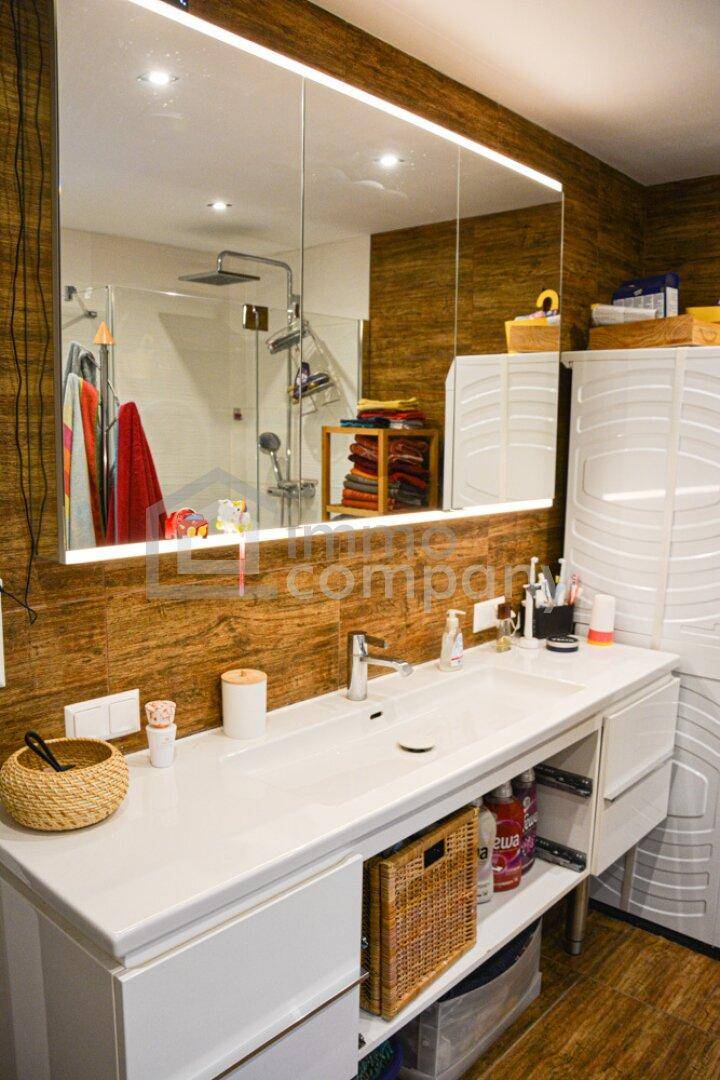 Modernes Badezimmer mit Doppelwaschbecken, großem beleuchteten Spiegel und begehbarer Dusche.