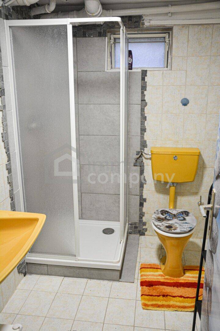 Einfaches Badezimmer im Keller mit Duschkabine, gelber Toilette und Fliesenboden.