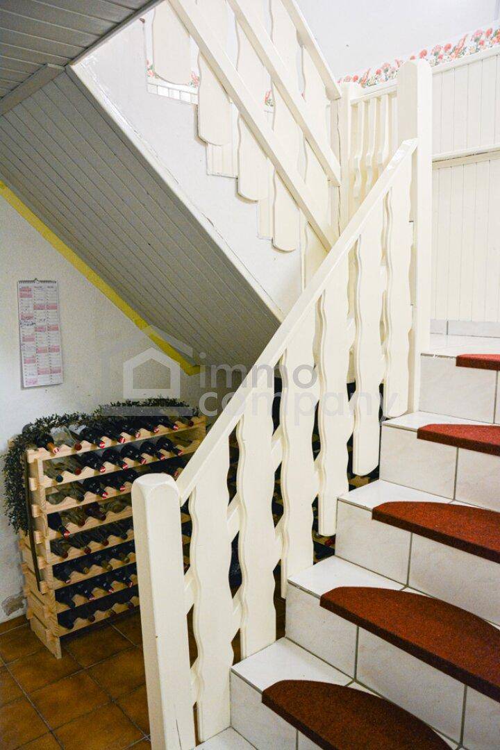 Treppenhaus mit weißem Holzgeländer, Teppichstufen und integriertem Weinregal.