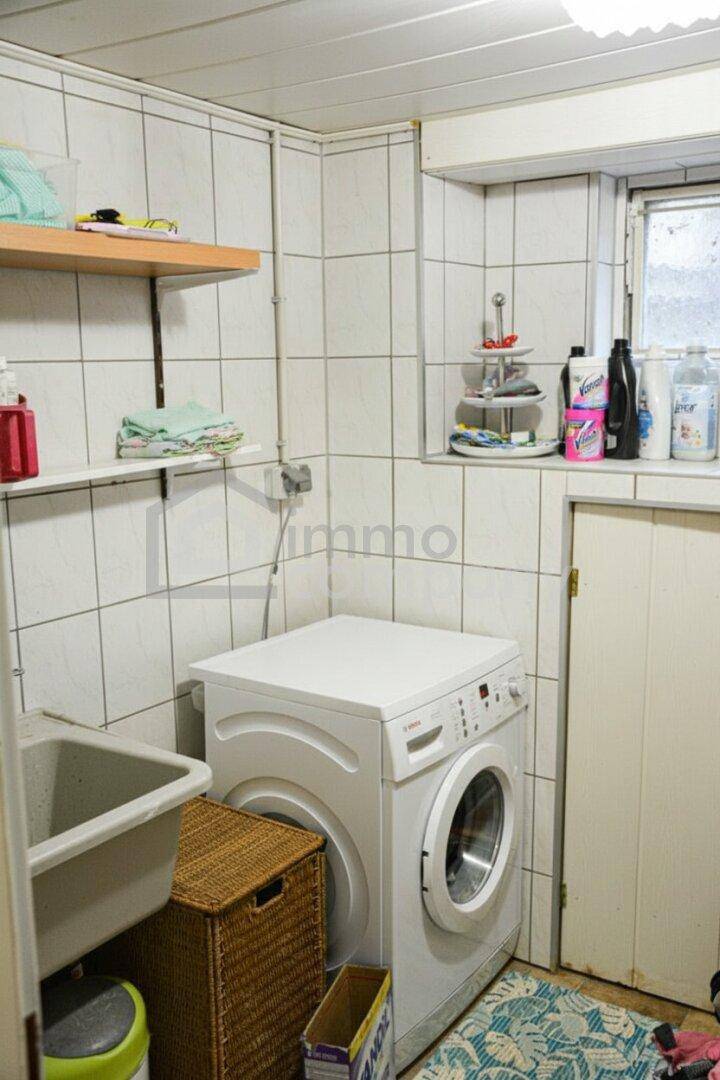 Praktische Waschküche mit Waschmaschine, Spülbecken und weißen Fliesenwänden.