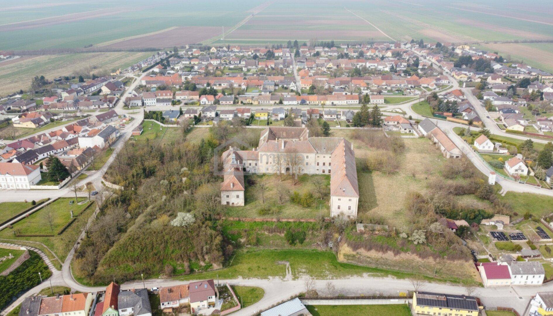 Luftaufnahme eines weitläufigen historischen Gebäudekomplexes umgeben von ländlicher Bebauung und Feldern.