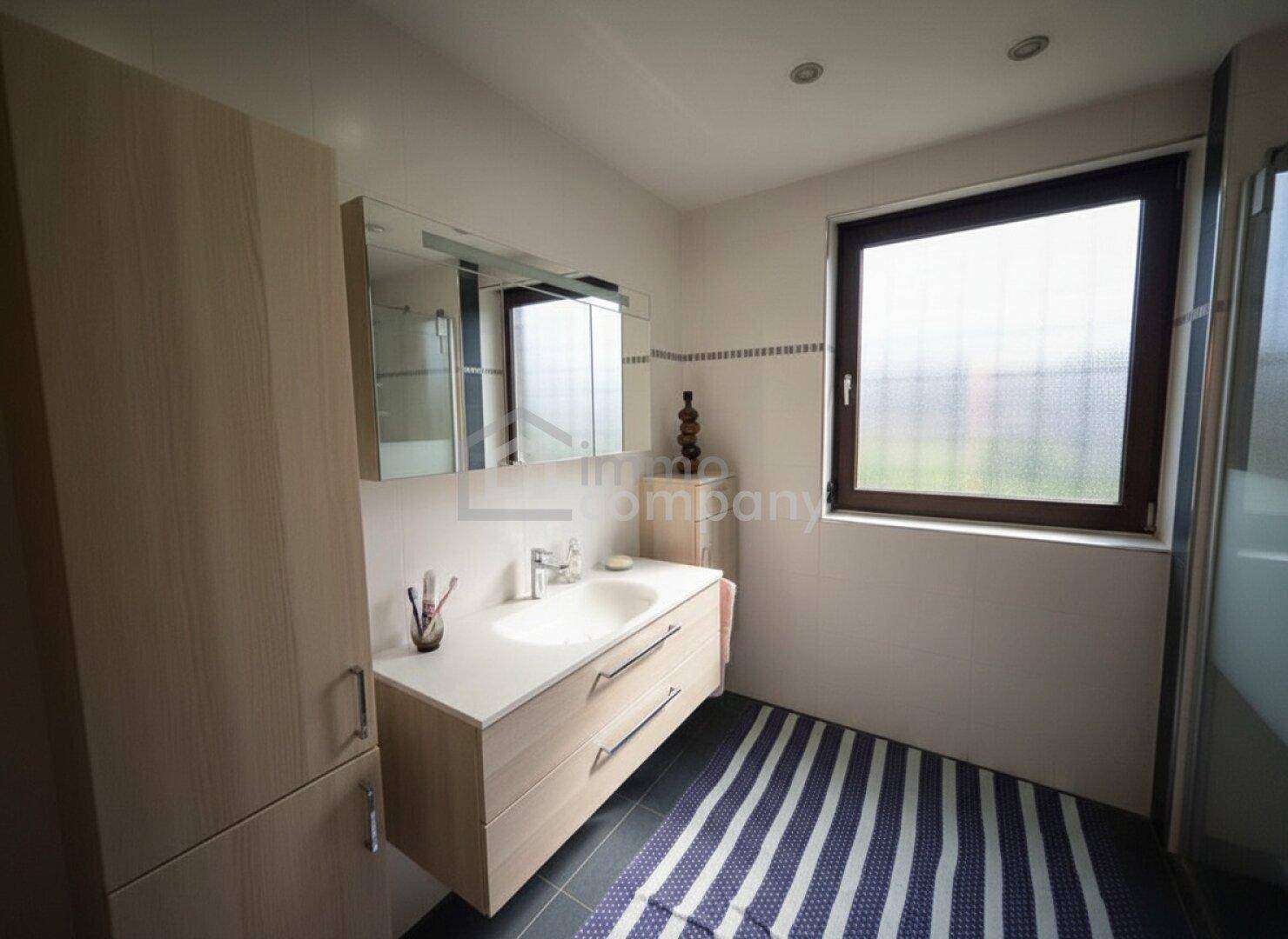 Helles Badezimmer mit Fenster, modernem Waschtisch und dunklem Fliesenboden.