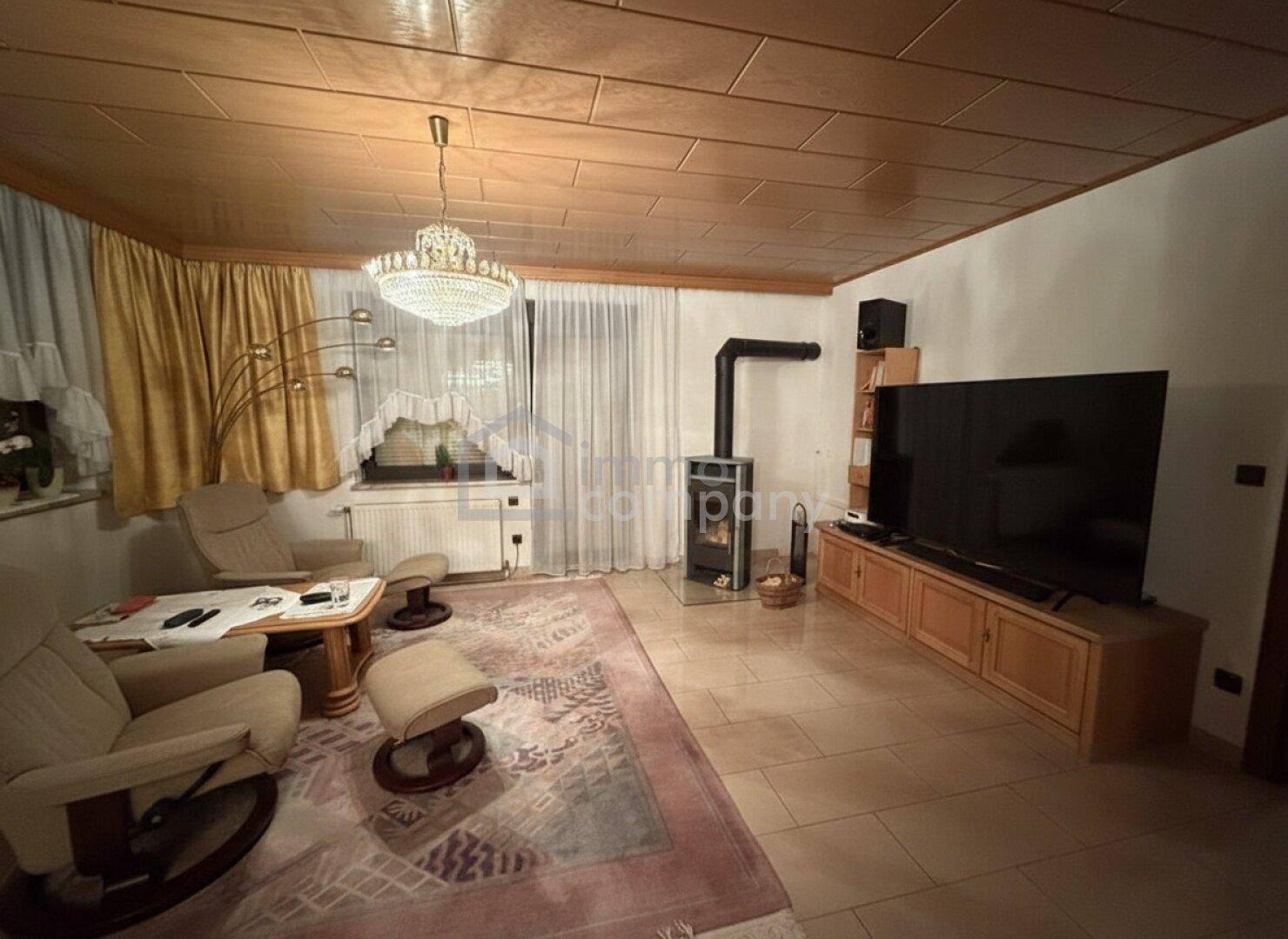 Wohnzimmer mit Kaminofen, bequemen Sesseln und Holzdecke, einladend gestaltet.