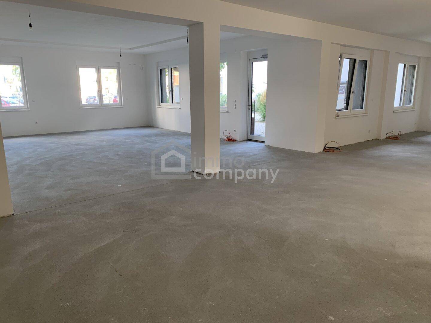Heller, offener Raum mit vielen Fenstern, Betonboden und tragenden Säulen, ideal für flexible Nutzung.