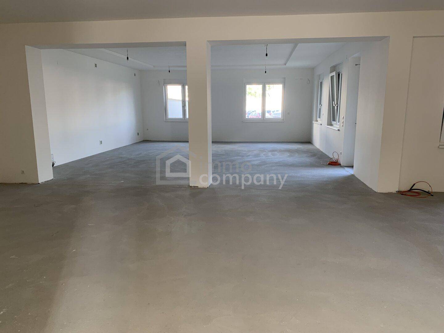 Geräumiger, offener Innenraum mit Betonboden und Säulen, ideal für individuelle Raumgestaltung.