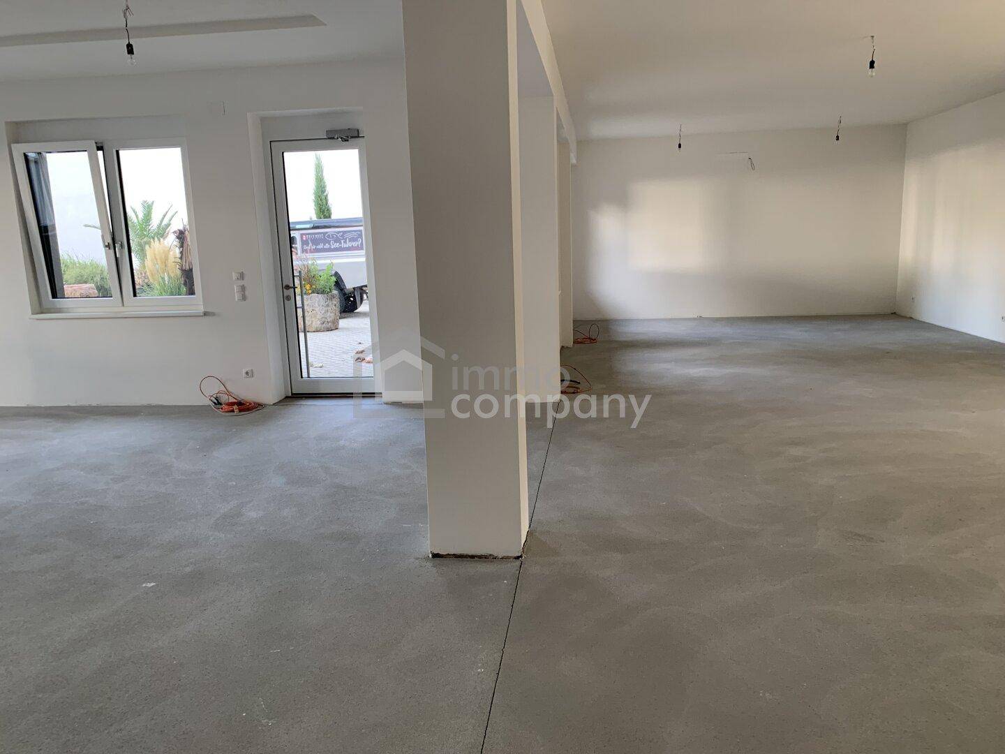 Heller, offener Raum mit Betonboden und Zugang zum Außenbereich, ideal für gewerbliche oder private Nutzung.