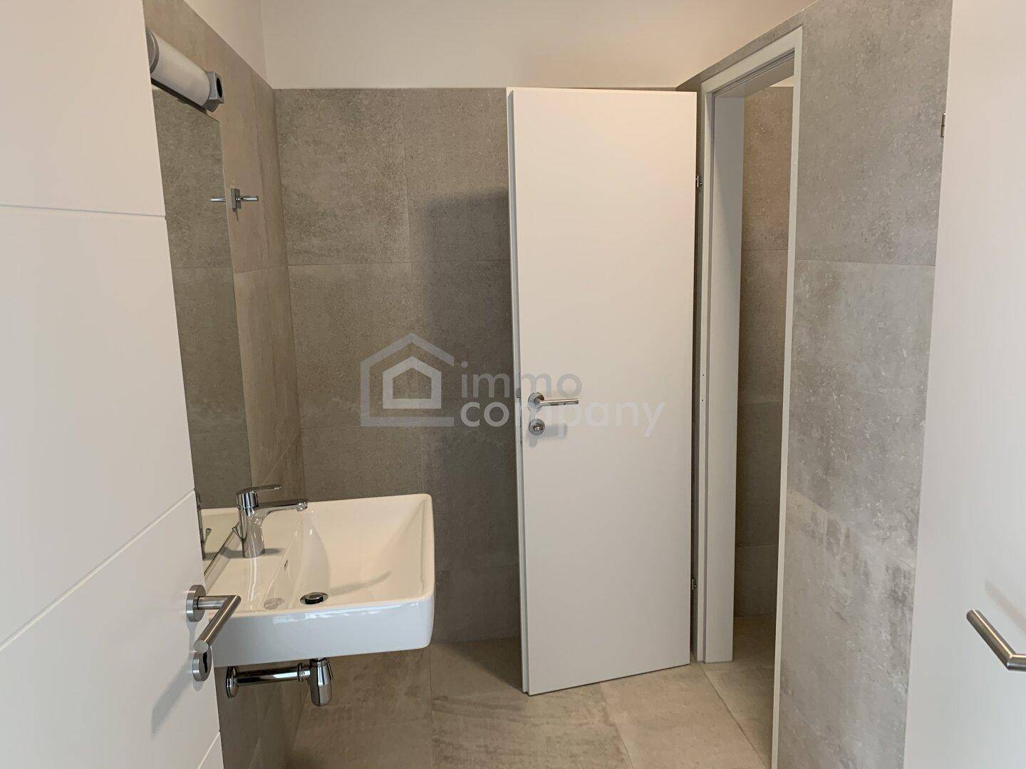 Modernes Badezimmer mit eleganten grauen Fliesen, einem stilvollen Waschbecken und weißer Tür.