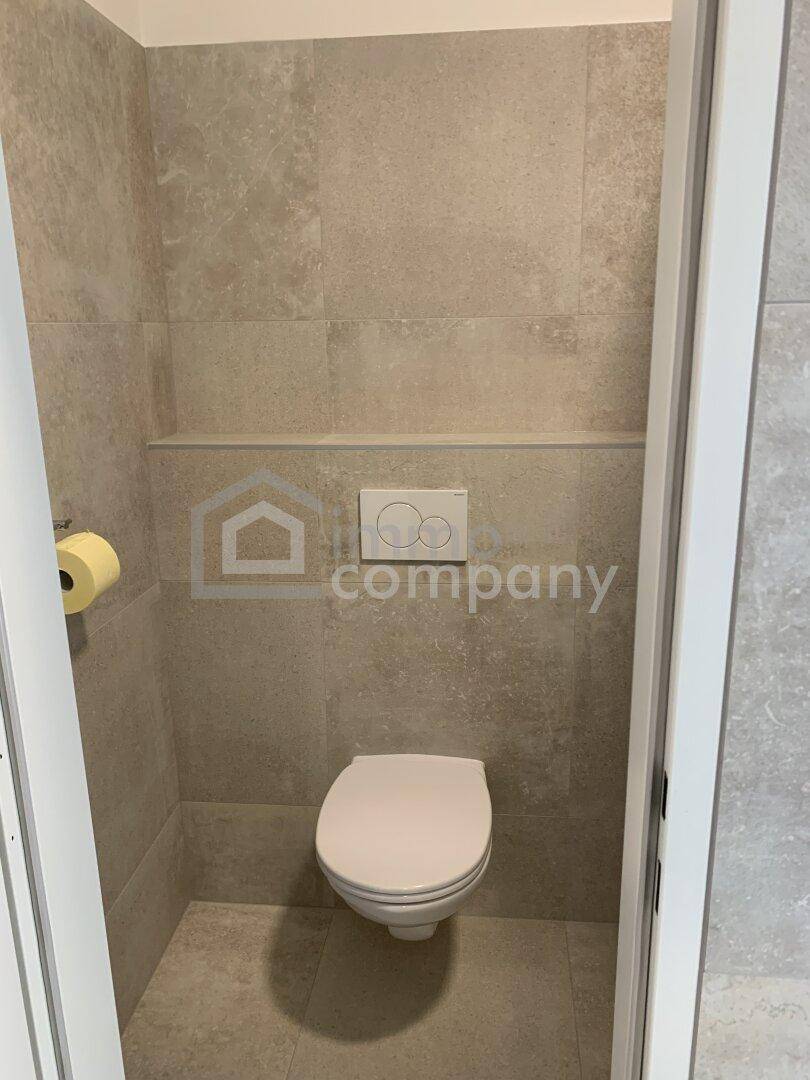 Gäste-WC mit wandhängender Toilette und modernen grauen Fliesen an Wänden und Boden.