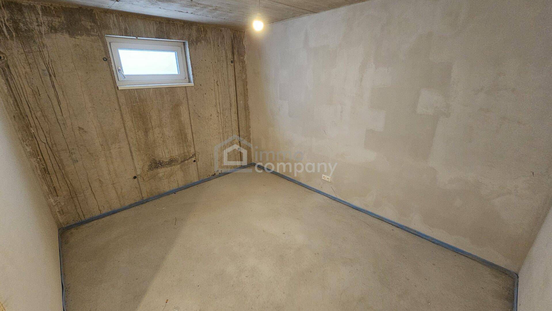 Kellerraum im Rohbau mit Betonwänden und einem kleinen Fenster, geeignet als Abstellraum.