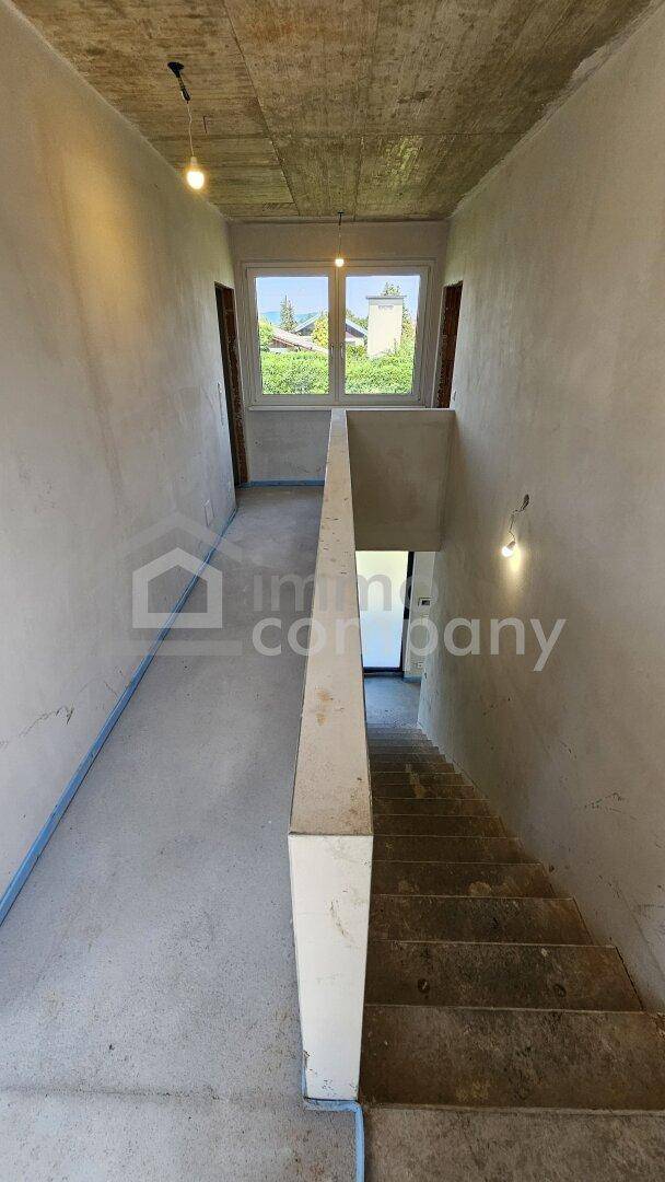 Treppenhaus im Rohbau mit Betonstufen und einem Fenster im oberen Bereich, das Licht spendet.
