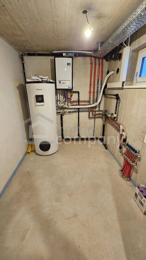 Technikraum im Keller mit Warmwasserspeicher, Rohren und elektrischen Installationen.
