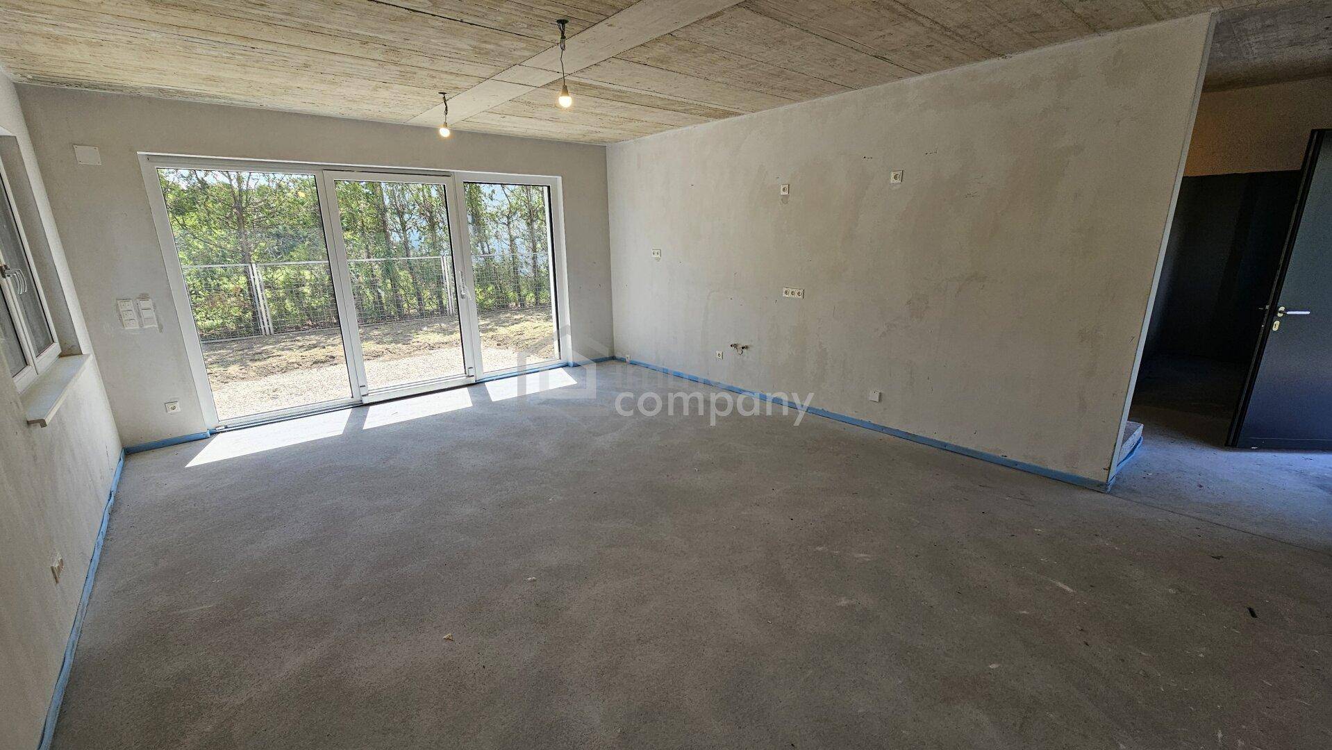 Geräumiges Wohnzimmer im Rohbau mit großen Schiebetüren, die viel Tageslicht hereinlassen.