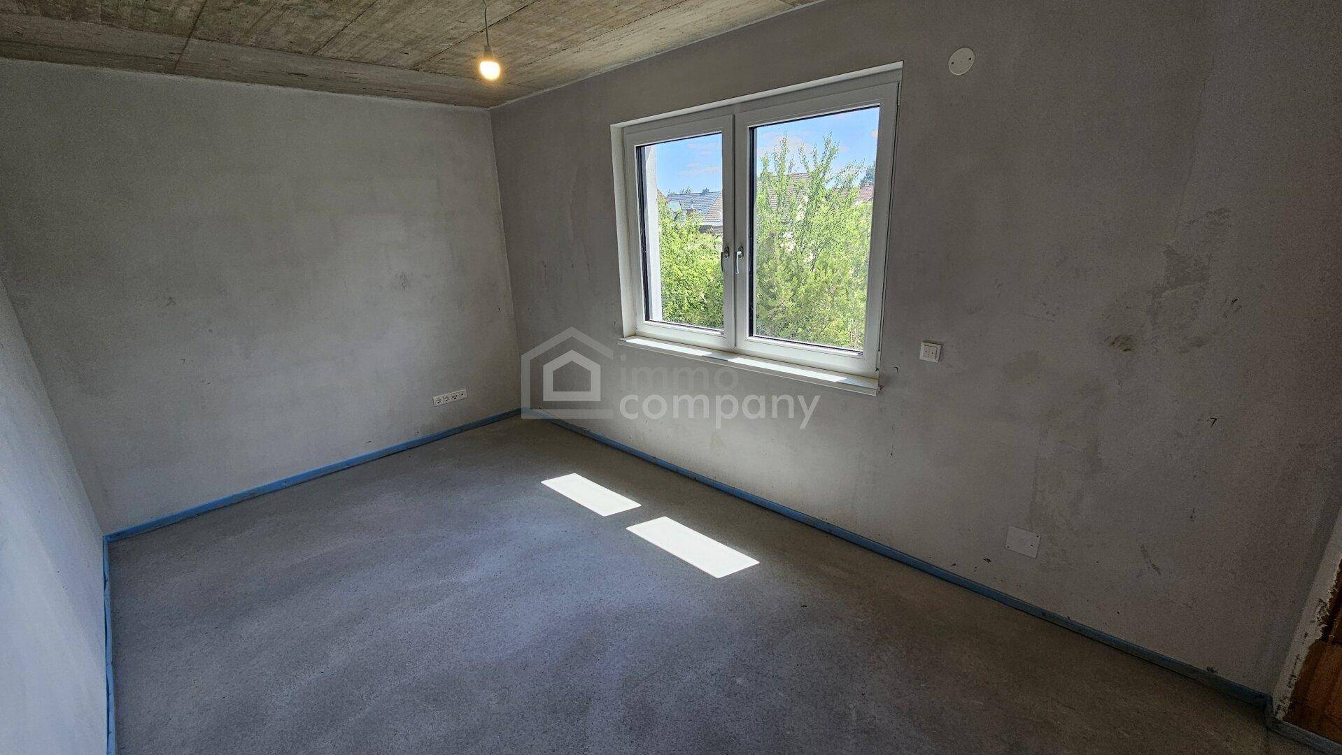 Helles Zimmer im Rohbau mit Fenster, Betonoptik an der Decke und viel natürlichem Tageslicht.