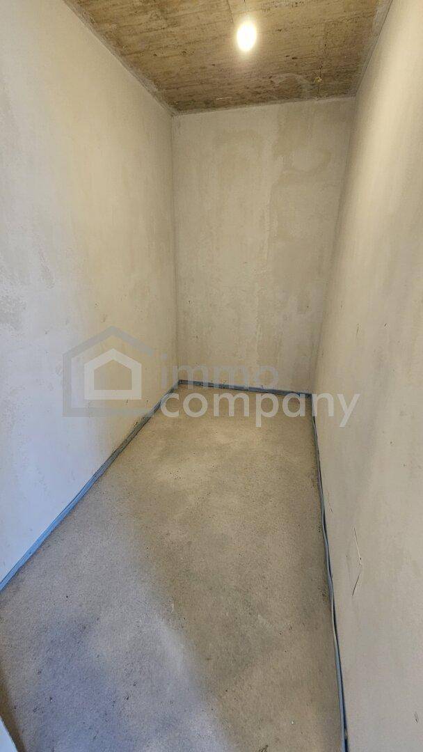 Unfertiger Raum im Rohbau mit Betonoptik an der Decke und einfachen Wänden, bereit für den Ausbau.